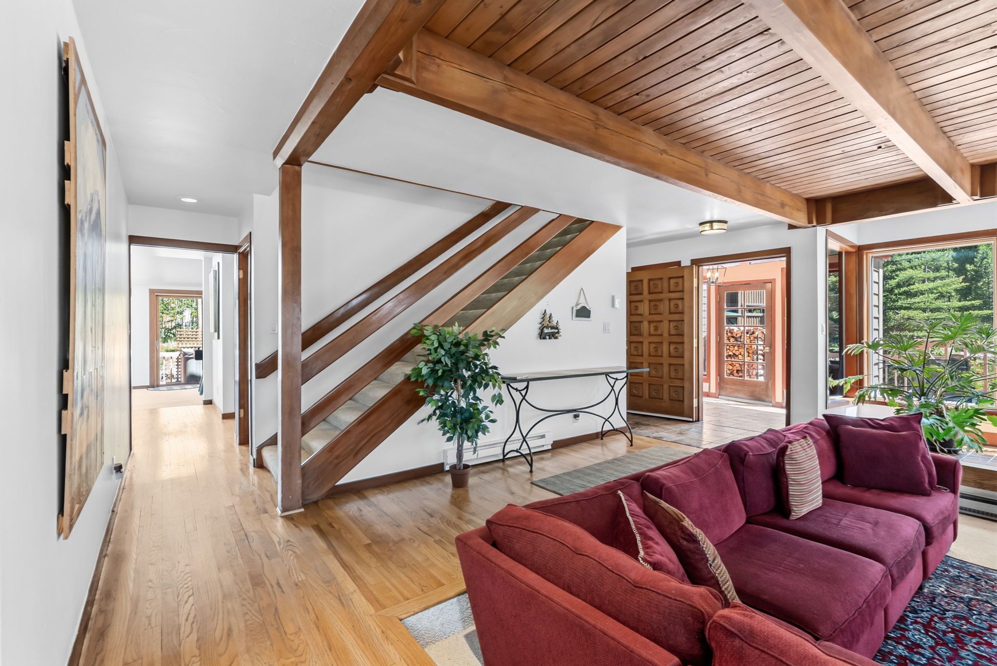 Un intérieur moderne avec un escalier en bois, un canapé rouge et une vue sur l’extérieur.