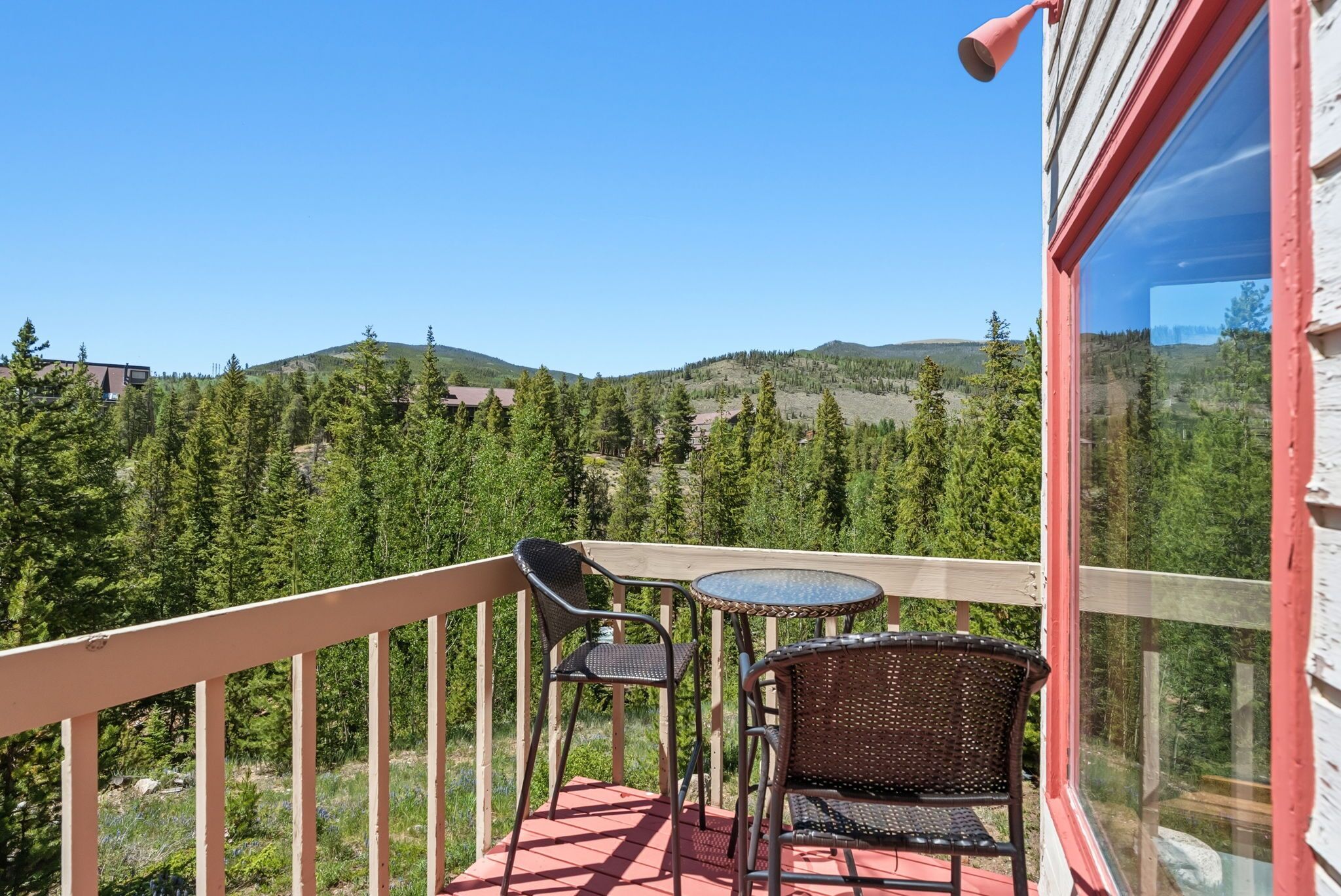 Un balcon avec une table et des chaises, donnant sur un paysage montagneux boisé.