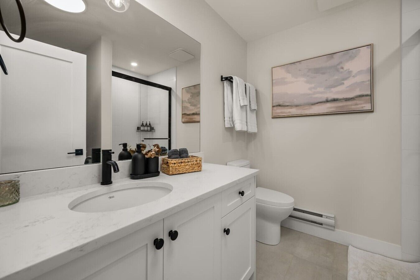 A modern bathroom with a white vanity, a large mirror, a toilet, and a wall-mounted towel rack.