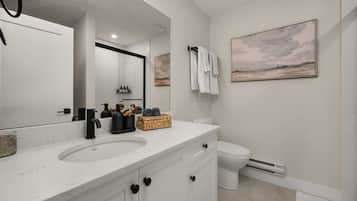 A modern bathroom with a white vanity, a large mirror, a toilet, and a wall-mounted towel rack.