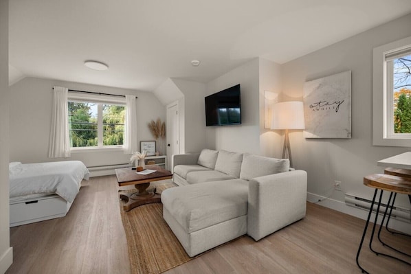 Un salon moderne avec un canapé, une table basse, un téléviseur fixé au mur et une fenêtre avec des rideaux.