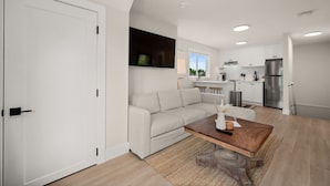 Un appartement moderne comprenant un espace de vie, un canapé, une table basse, une cuisine avec des meubles blancs et un réfrigérateur.