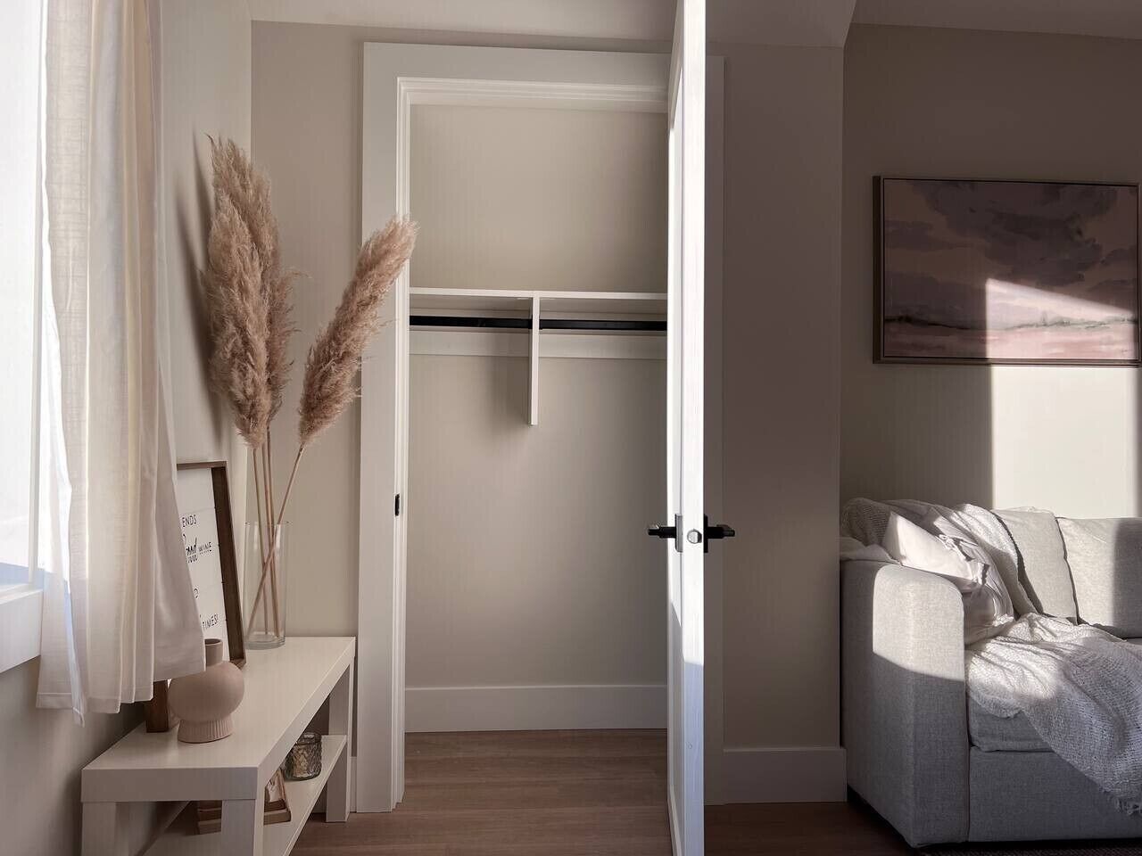 A room with a white door, a sofa, a small table with a vase, and pampas grass.