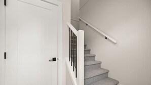 Un escalier avec une rampe blanche et des marches recouvertes de moquette, menant à une porte blanche fermée.