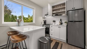 A modern kitchen with white cabinetry, a stainless steel refrigerator, and a window with a view of trees.