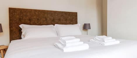 A neatly made bed with white linens and towels, a brown headboard, and a bedside lamp.