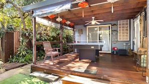 An outdoor deck with a pool table, wooden chairs, and a ceiling fan.