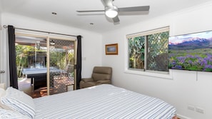 A bedroom with a bed, a chair, a ceiling fan, a window with a view, and a door leading to an outdoor area.