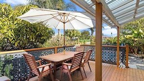 An outdoor patio with a wooden table and chairs, a white umbrella, and a decorative fence. - Private Oasis with pool, BBQ & entertaining areas (The Entrance)