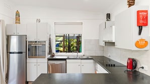 Una cocina moderna con electrodomésticos de acero inoxidable, una ventana con vistas a zonas verdes y una manta ignífuga roja en la pared.