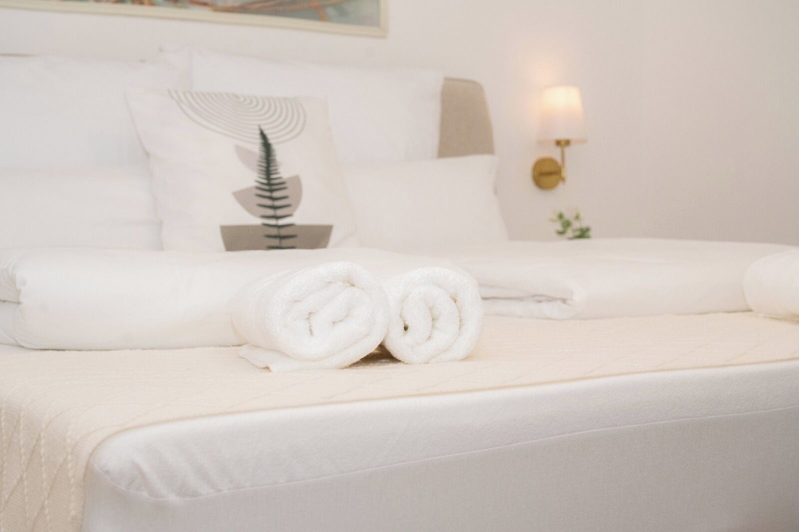 Een hotelkamer met een net opgemaakt bed, witte beddengoed en een wandlamp.