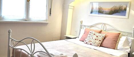 Una cama bien hecha con un edredón estampado, una mesita de noche con lámpara y una ventana con cortinas.