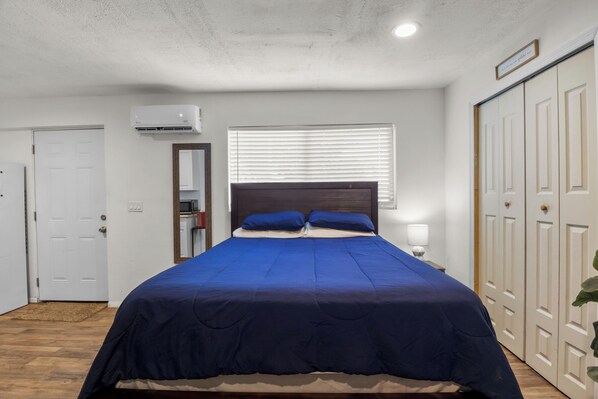 A bedroom with a bed, a window with blinds, a door, and an air conditioning unit.