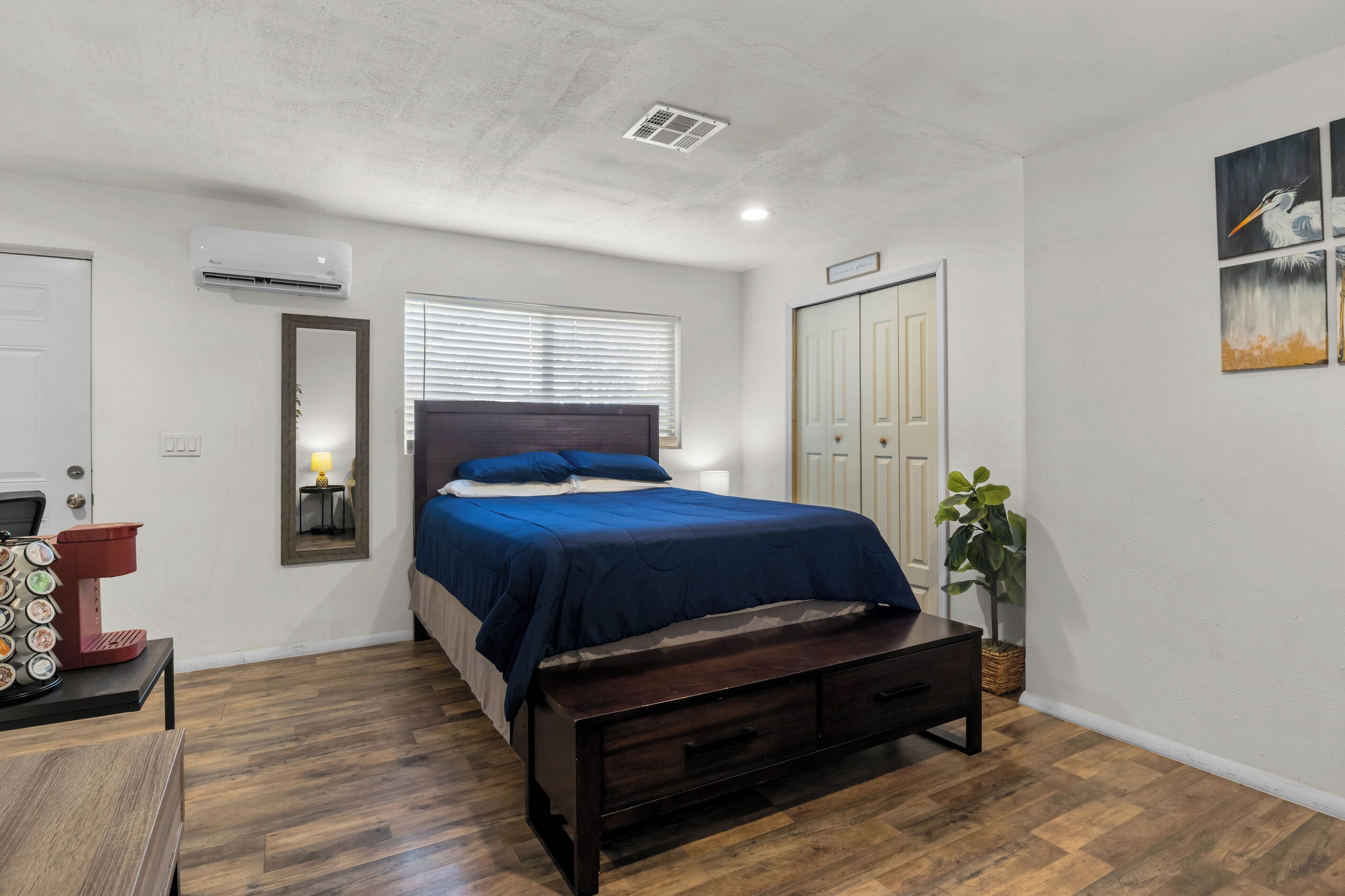 Ein Schlafzimmer mit Bett, Nachttisch, Spiegel, Kleiderschrank und einer Zimmerpflanze.