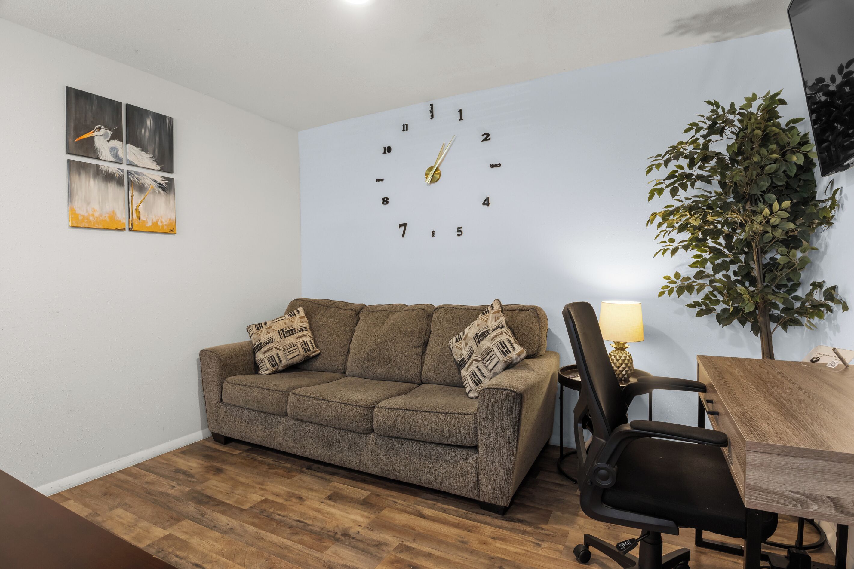 Un salon avec un canapé, un fauteuil, une horloge et une plante.