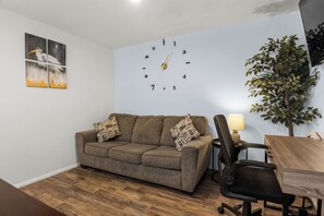 A living room with a sofa, a chair, a clock, and a plant.
