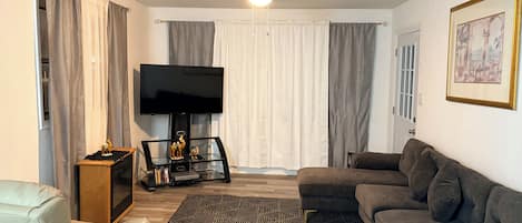 A living room with a sofa, a television, a ceiling fan, and a patterned rug.