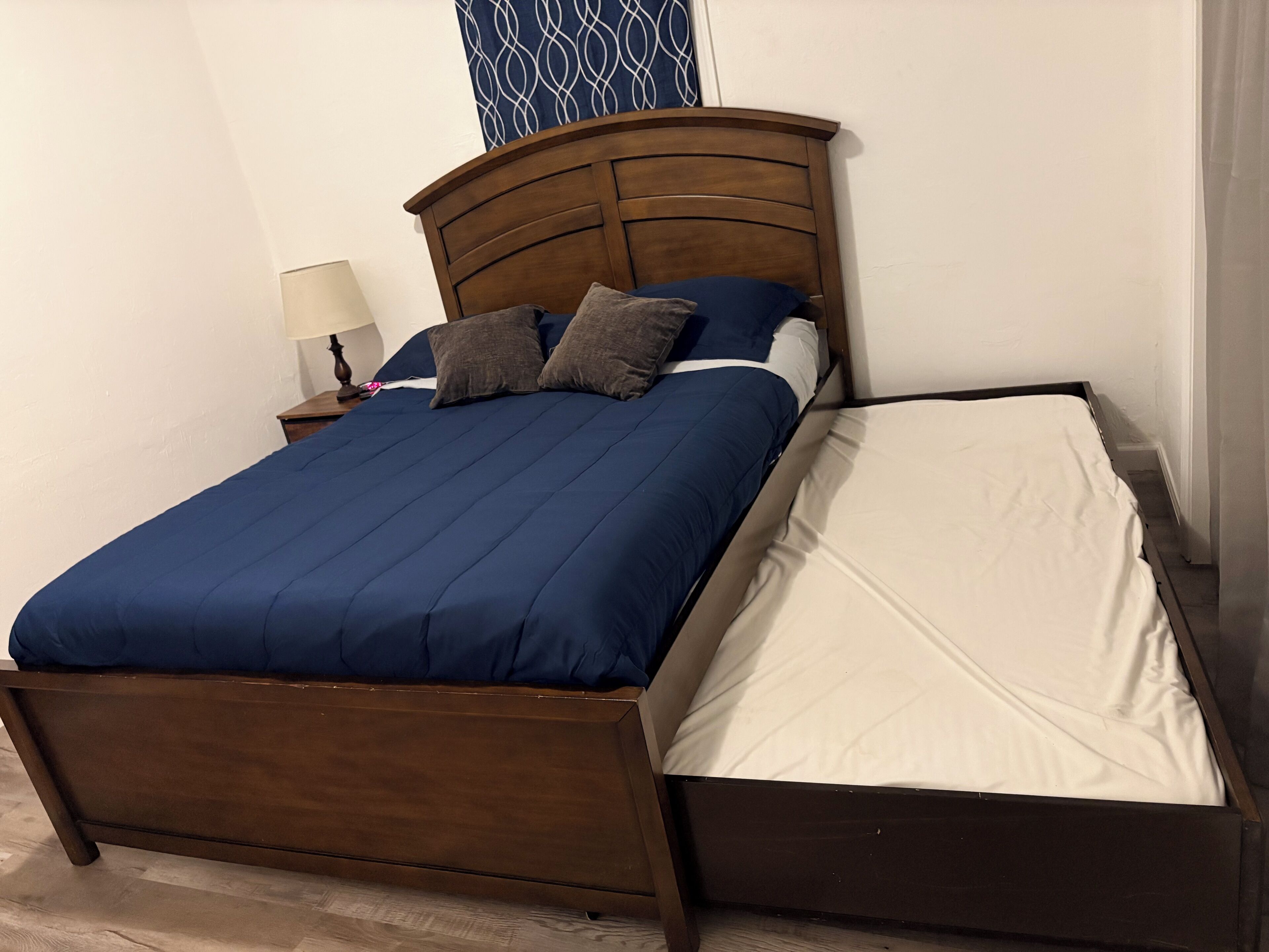A single bed with a wooden headboard, a blue bedspread, and two pillows.