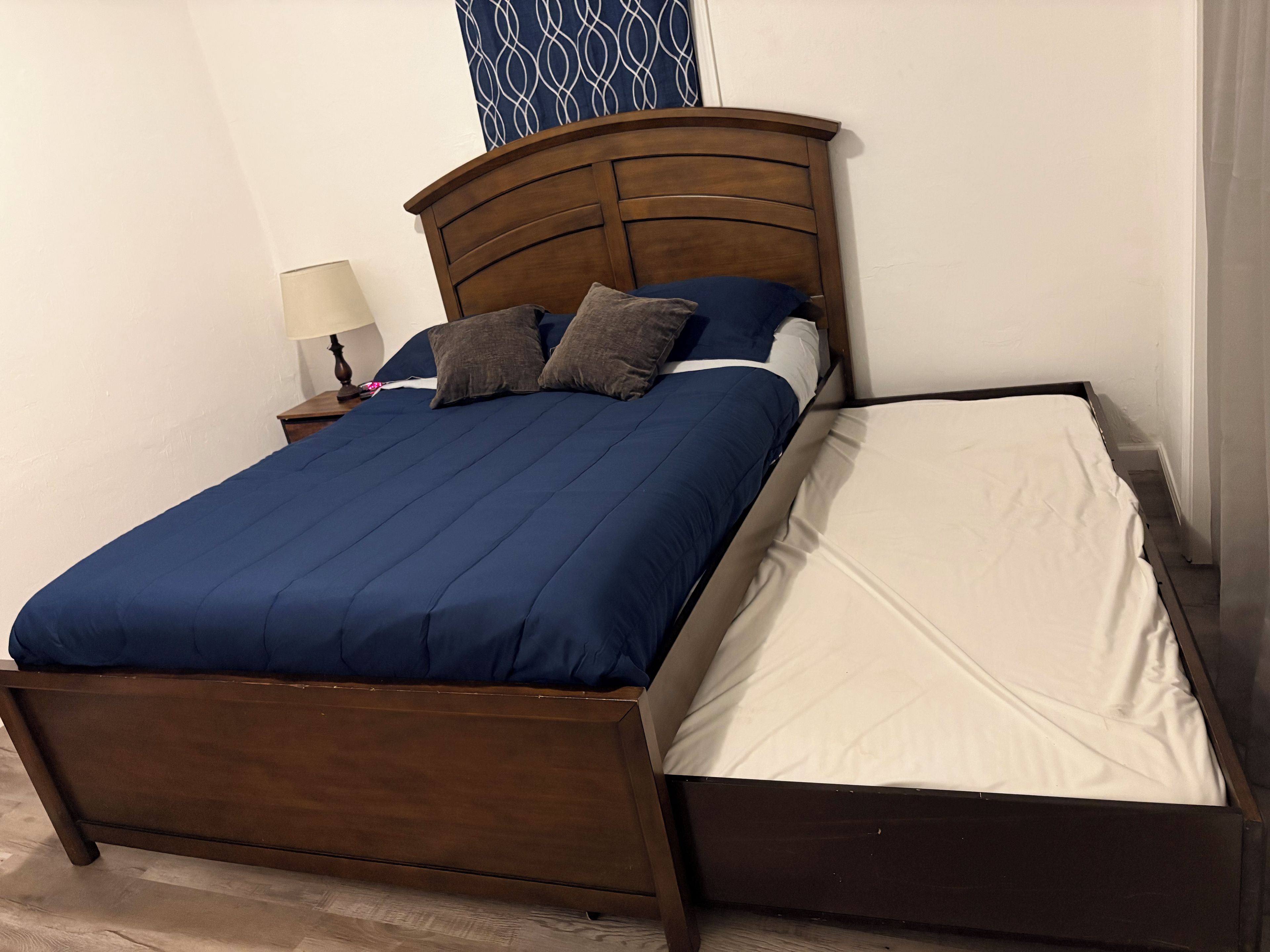 A bed with a wooden frame, a blue bedspread, and two pillows.