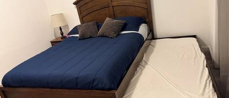 A bed with a wooden frame, a blue bedspread, and two pillows.