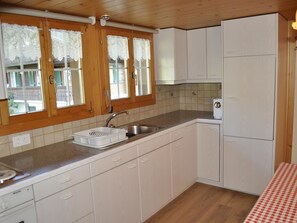 Eine Küche mit Holzausstattung, einem Spülbecken und einem Fenster mit Spitzenvorhängen.