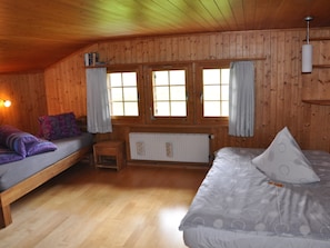 Eine Holzhütte mit zwei Betten, einem kleinen Tisch und einem Fenster mit Vorhängen.