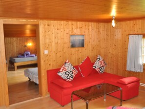 Ein Zimmer mit einem roten Sofa, einem Glastisch, Holzwänden, einem Bett und einem Gemälde.
