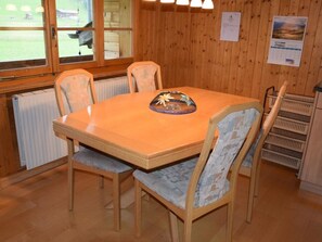 Ein Zimmer mit Holzwänden, einem Tisch in der Mitte und vier Stühlen, sowie einer Heizung.