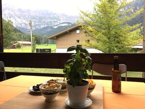 Ein Tisch mit einem Blumentopf, Schalen mit Snacks und einer Bierflasche, im Hintergrund eine Bergblick.