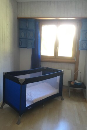 Ein Zimmer mit einem Etagenbett, einem Vorhangfenster, einem Heizkörper und einem kleinen Tisch mit einer Lampe.