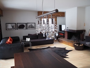 A modern living room with a black sofa, a wooden coffee table, a fireplace, and a chandelier. - Rothenbach Appartement/Fewo, Dusche oder Bad, WC, 3 Schlafräume 6-Bettwohnung by Interhome (Lenk)