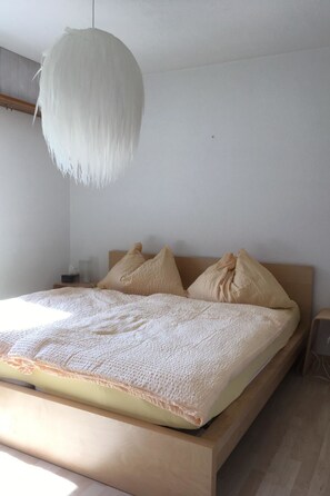 Ein schlicht eingerichtetes Schlafzimmer mit einem Holzbett, einer weißen, strukturierten Decke und einer Pendelleuchte.