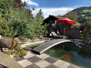 A wooden deck leading to a pond with a small bridge, surrounded by greenery and a mountain backdrop. - Strubeli Appartement/Fewo, Dusche oder Bad, WC, 2 Schlafräume 4-Bett-Wohnung by Interhome (St Stephan)