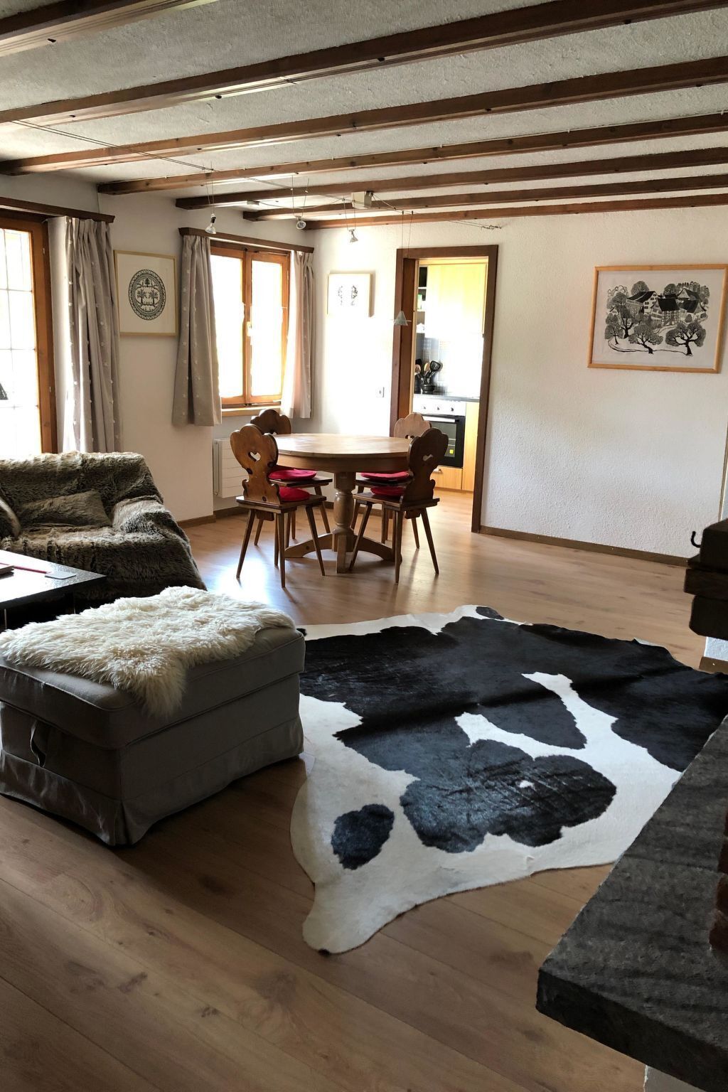 A room with a dining table, chairs, a sofa, a fur-covered ottoman, and a cowhide rug.