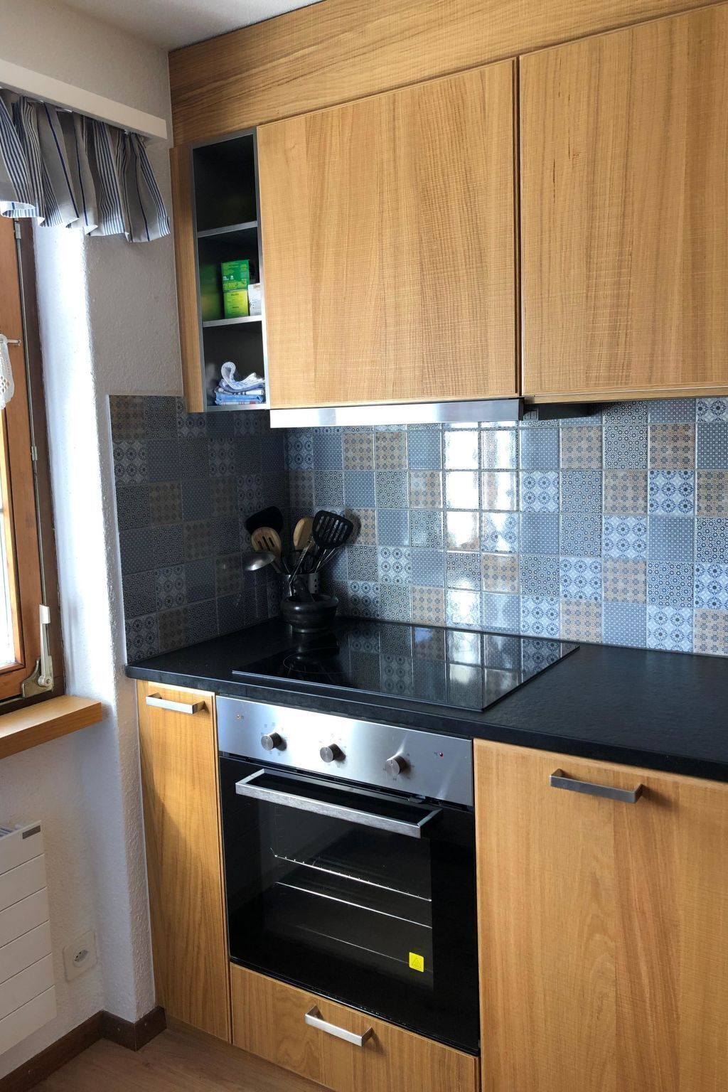 A compact kitchen with wooden cabinets, a black countertop, and patterned backsplash tiles.