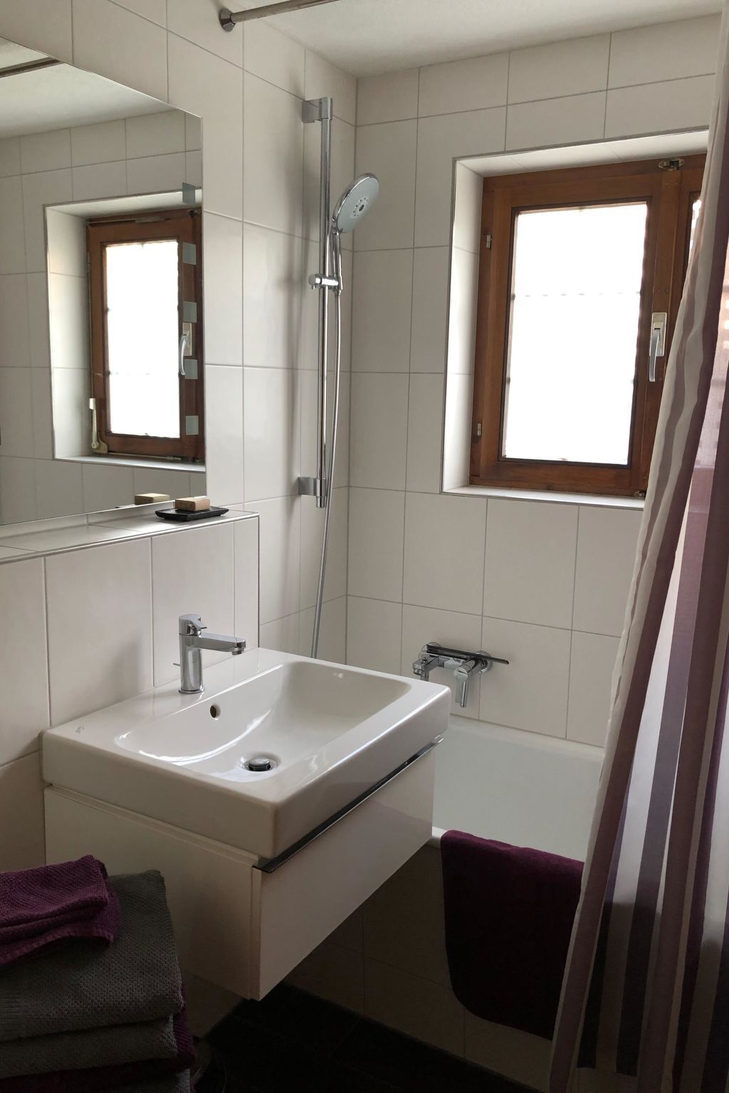 A bathroom with a white sink, a mirror, a shower, and a window.
