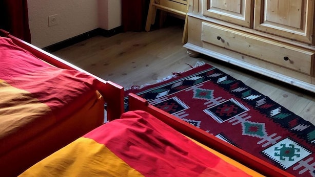 Une pièce comprenant un lit, une armoire, une fenêtre avec des rideaux et un tapis à motifs.