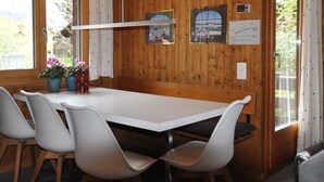 A wooden-paneled room with a white table and chairs, a hanging light fixture, and a window with curtains. - Sumpfbödeli Appartement/Fewo, Badewanne, 3 Schlafräume 6-Bett-Wohnung by Interhome (Lenk)