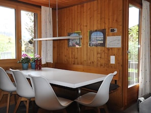 Ein Zimmer mit Holzwänden, einem weißen Tisch und Stühlen, einer Pendelleuchte und einem Fenster mit Vorhängen.