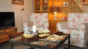 A cozy living room with floral-patterned chairs, a coffee table with snacks, a television, and a bookshelf. - Sumpfbödeli Appartement/Fewo, Badewanne, 3 Schlafräume 6-Bett-Wohnung by Interhome (Lenk)