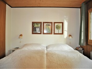 A double bed with a white duvet in a room with wooden walls and a wooden ceiling. There are three framed pictures on the wall above the bed. - Sumpfbödeli Appartement/Fewo, Badewanne, 3 Schlafräume 6-Bett-Wohnung by Interhome (Lenk)