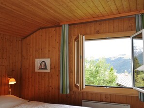 Ein Zimmer mit Holzwänden, einem Bett, einem Fenster mit Vorhängen und einem gerahmten Bild an der Wand.