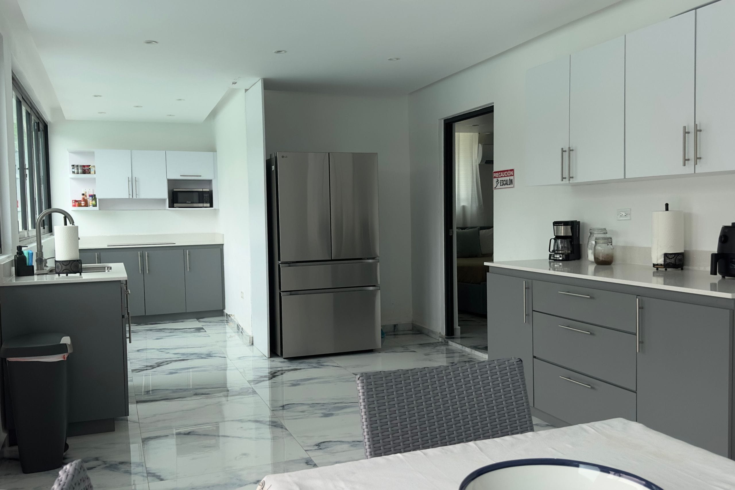 A modern kitchen with a stainless steel refrigerator, white cabinets, and a marble floor.