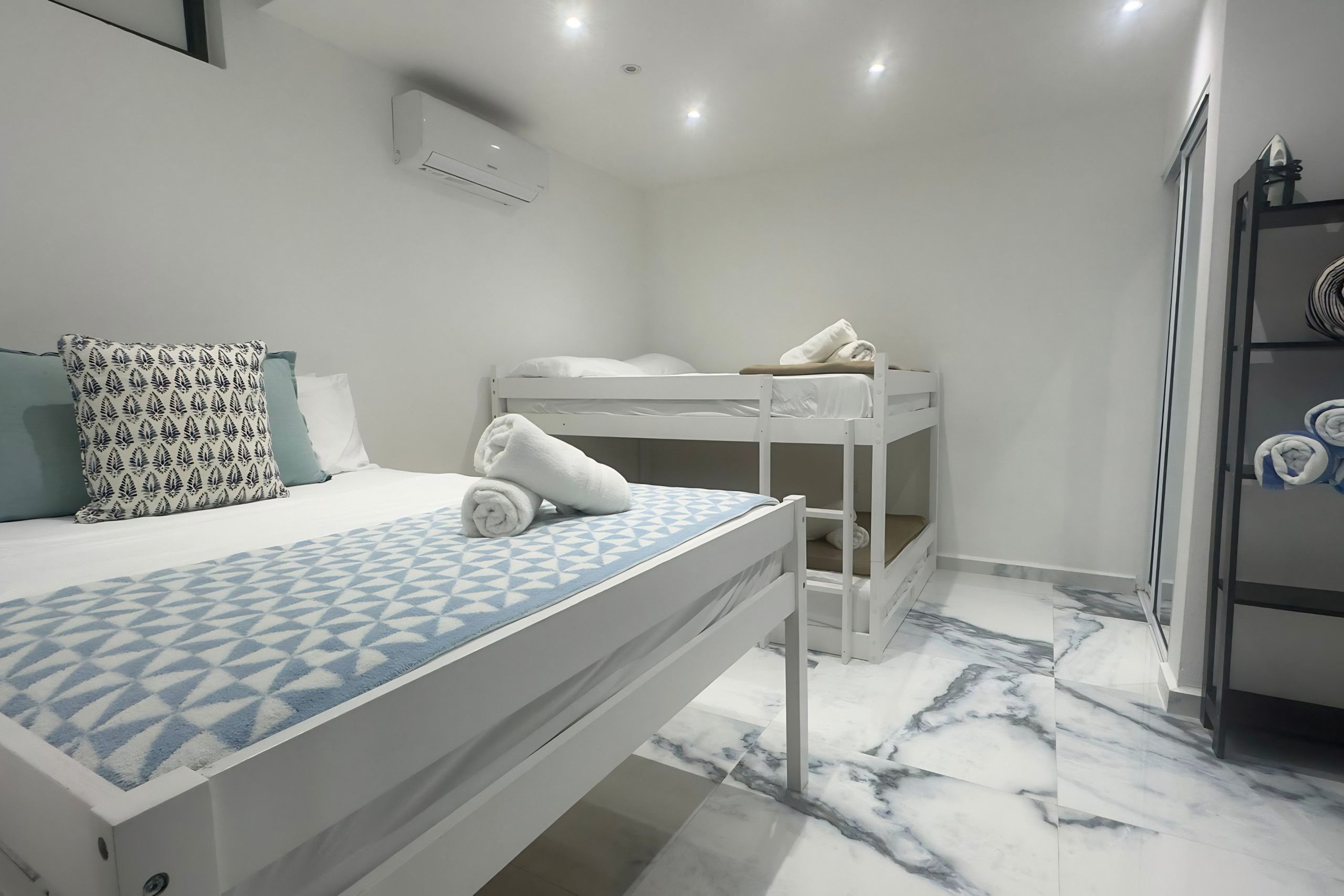 A bedroom with a bunk bed, a single bed with patterned pillows, and a marble floor.