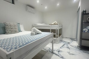 A bedroom with a bunk bed, a single bed with patterned pillows, and a marble floor.