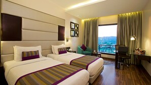 A hotel room with two beds, a desk, a chair, a laptop, and a view of the outdoors.