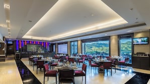 A modern restaurant with a high ceiling, large windows, and a flat-screen TV.