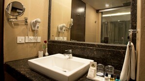 A hotel bathroom with a large sink, a mirror, a hairdryer, and toiletries on the counter.