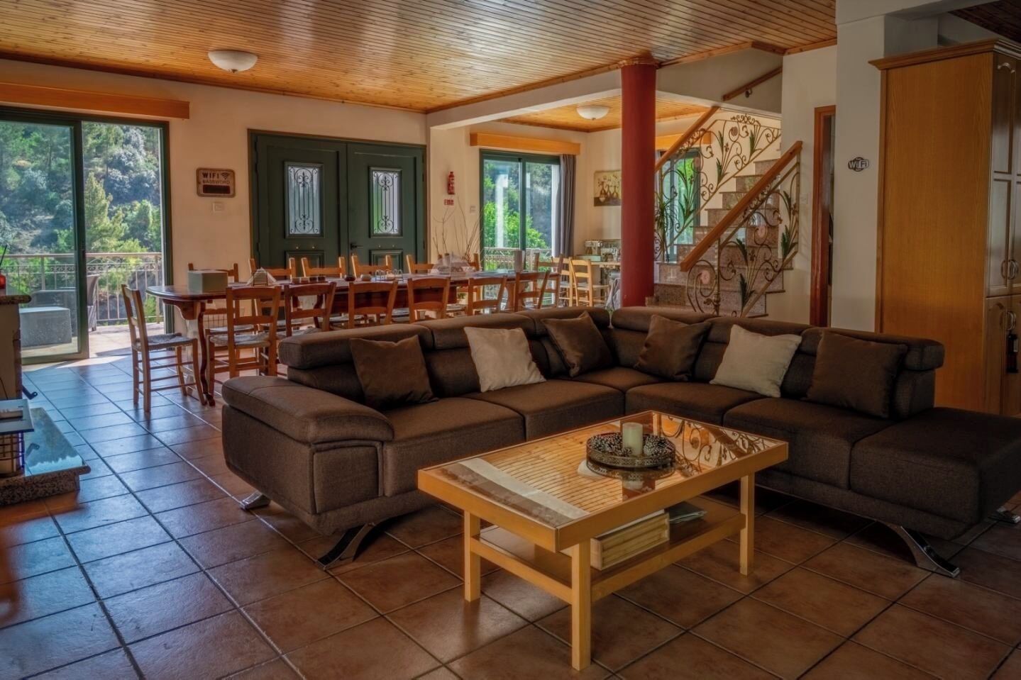 A spacious living area with a large sectional sofa, a wooden coffee table, and a dining area with wooden chairs and a table.