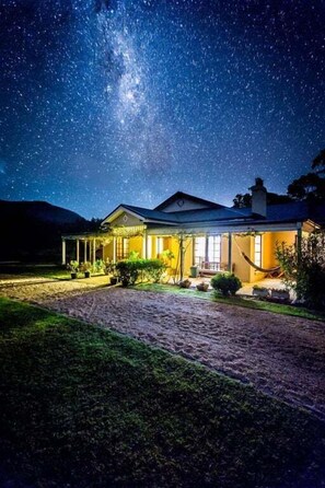 A house with a well-lit exterior, a paved driveway, and a starry night sky. - Wahroonga Luxury Estate in Kangaroo Valley (Kangaroo Valley)